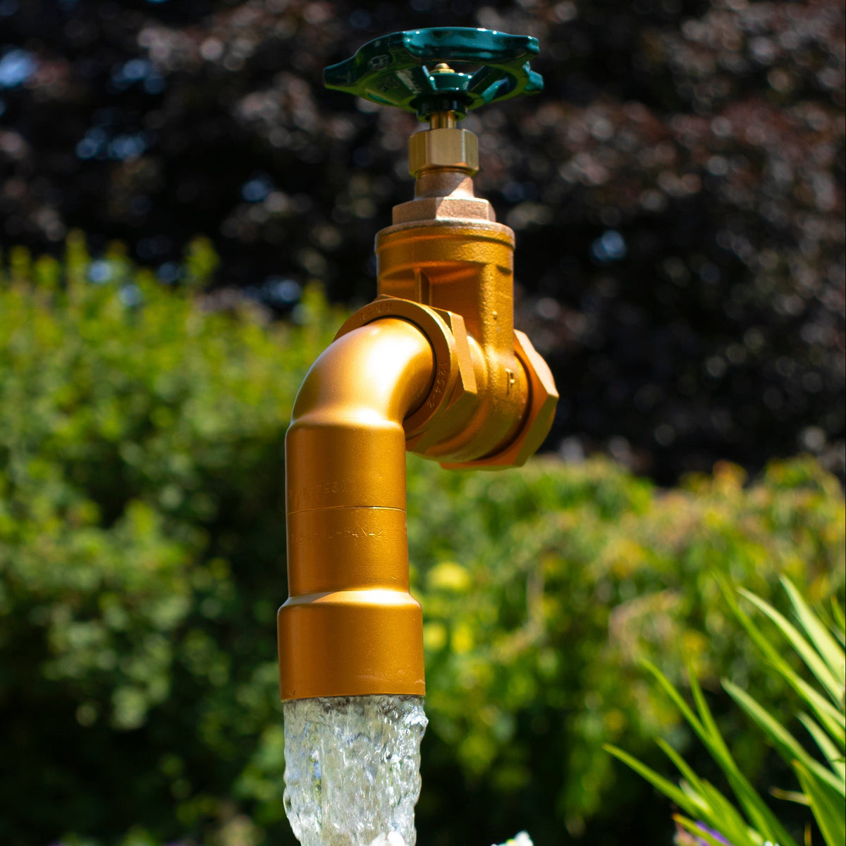 A large floating tap installed on top of a barrel surrounded by plants, with a clear sky and trees in the background.